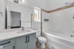 Bathroom featuring a spacious vanity with a white countertop and gray cabinetry, an integrated sink with a chrome faucet, a large wall-mounted mirror, and a tub/shower combination with a tiled surround - 