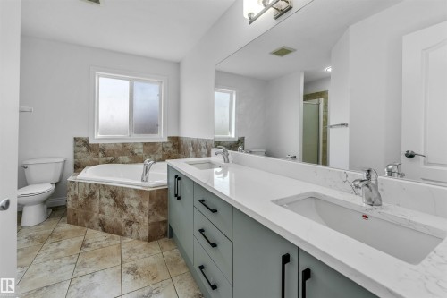 Bathroom featuring a double vanity with light gray cabinetry and white countertops, a large mirror, a built-in corner bathtub with tiled surround, and patterned floor tiling - 16205 55 Street Nw, Edmonton, AB - Indoor Photo Showing Bathroom