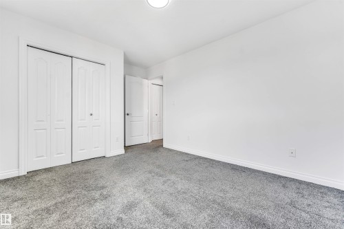 Neutral white wall finishes, crisp white trim, and bi-fold closet doors - 16205 55 Street Nw, Edmonton, AB - Indoor Photo Showing Other Room