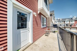 Private concrete balcony with black metal railing, featuring a white exterior door with glass insert, red horizontal siding, and an exterior wall sconce - 