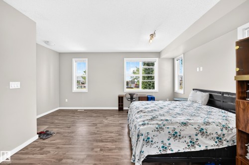 Spacious interior featuring wood-finish flooring, multiple windows, and light gray wall tones - #10 2803 James Mowatt Trail Sw, Edmonton, AB - Indoor Photo Showing Bedroom