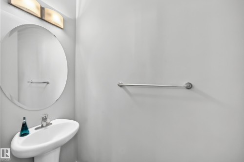 Pedestal sink featuring a chrome faucet, large circular mirror, and overhead vanity lighting - #10 2803 James Mowatt Trail Sw, Edmonton, AB - Indoor Photo Showing Bathroom