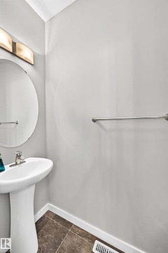 Pedestal sink with chrome faucet, complemented by a large circular mirror and modern wall-mounted lighting - #10 2803 James Mowatt Trail Sw, Edmonton, AB - Indoor Photo Showing Bathroom