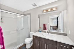 Bathroom featuring a glass-enclosed shower, a vanity with a white countertop and integrated sink, a large wall-mounted mirror, and a three-light fixture - 