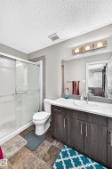 Bathroom featuring a glass-enclosed shower, a vanity with a white countertop and integrated sink, a large wall-mounted mirror, and a three-light fixture - 