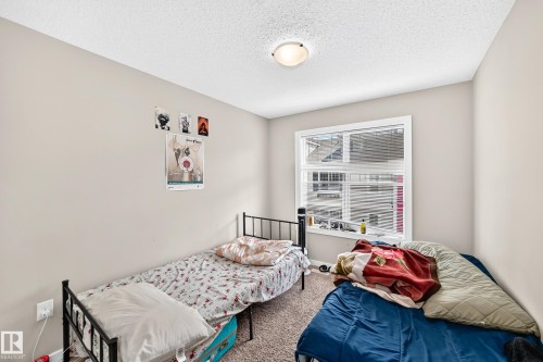Bedroom featuring a large window with white blinds, neutral wall paint, and textured ceiling - #10 2803 James Mowatt Trail Sw, Edmonton, AB - Indoor Photo Showing Bedroom