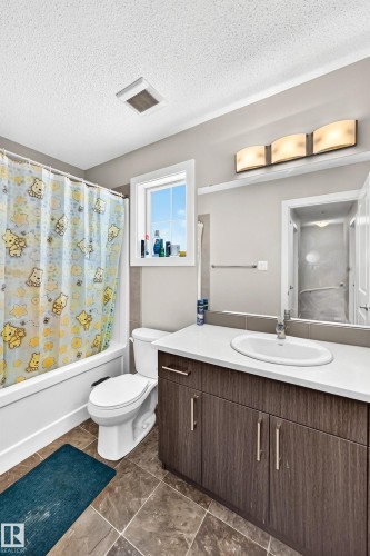 Contemporary bathroom featuring a wood-finish vanity with a white countertop and undermount sink, a large wall-mounted mirror, and tile flooring - #10 2803 James Mowatt Trail Sw, Edmonton, AB - Indoor Photo Showing Bathroom