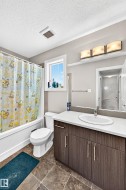 Contemporary bathroom featuring a wood-finish vanity with a white countertop and undermount sink, a large wall-mounted mirror, and tile flooring - 