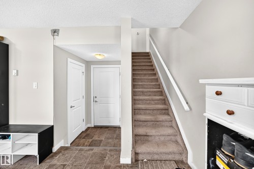Carpeted staircase with white handrail, leading from a tiled entryway featuring a white interior door and a flush-mount ceiling light fixture - #10 2803 James Mowatt Trail Sw, Edmonton, AB - Indoor Photo Showing Other Room