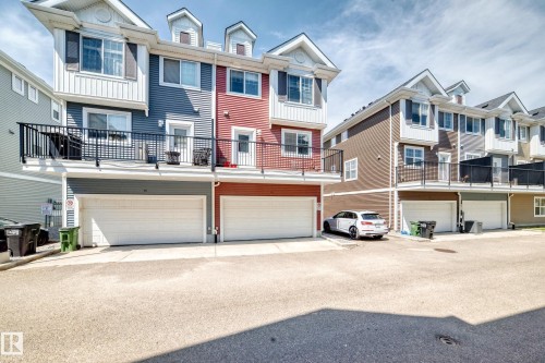 Exterior townhouse facade featuring multiple dormer windows, individual balconies with black railings, and attached garages with white doors - #10 2803 James Mowatt Trail Sw, Edmonton, AB - Outdoor With Balcony With Facade