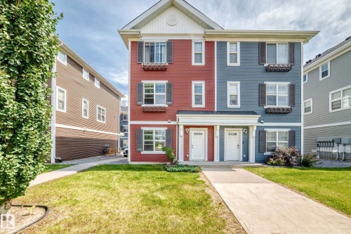 Modern townhome architecture featuring red and blue siding, white trim, and dark window shutters - #10 2803 James Mowatt Trail Sw, Edmonton, AB - Outdoor With Facade