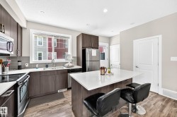 Modern kitchen featuring a central island with a solid surface countertop, wood-finish flooring, dark wood cabinetry, a grey subway tile backsplash, and stainless steel appliances - 