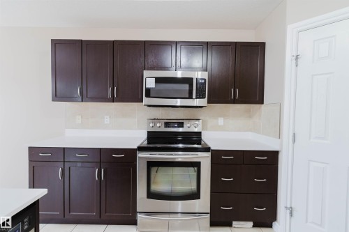 Modern kitchen featuring dark wood-finish cabinetry, white countertops, and a tiled backsplash - 1919 Hammond Place, Edmonton, AB - Indoor Photo Showing Kitchen