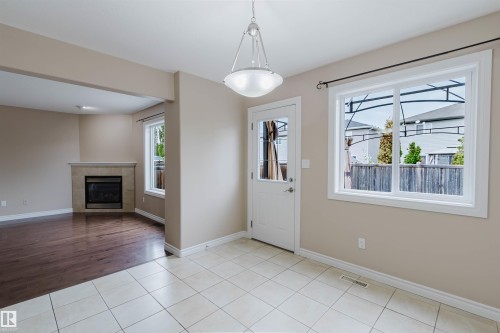 Dining area featuring light-toned tile flooring, pendant lighting, and a window with white trim - 1919 Hammond Place, Edmonton, AB - Indoor With Fireplace