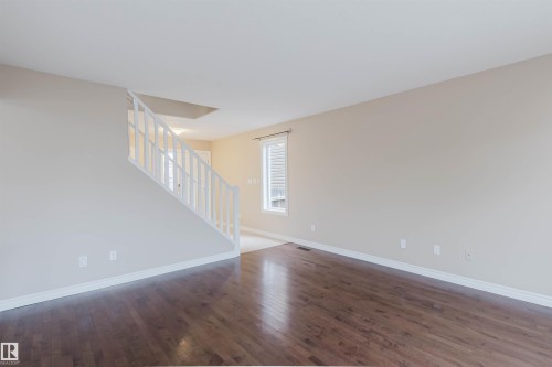 Spacious interior featuring dark wood-finish flooring, light neutral-toned walls, and white baseboards - 1919 Hammond Place, Edmonton, AB - Indoor Photo Showing Other Room