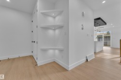 Built-in corner shelving with recessed lighting, wood-finish flooring, white baseboards, and matte black door hardware - 