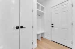 Entryway mudroom featuring white built-in storage with hooks and shelving, wood-finish flooring, and white paneled doors with black hardware - 