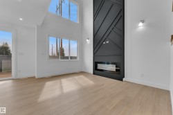 Expansive interior featuring a contemporary fireplace with a textured black surround, wood-finish flooring, and high ceilings - 