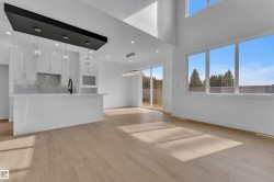 Open-concept living area featuring a modern kitchen island, wood-finish flooring, high ceilings, large windows, and sliding glass doors - 