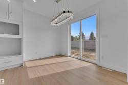 Bright interior featuring wood-finish flooring, a contemporary chandelier, and white built-in cabinetry with glass-front accents - 