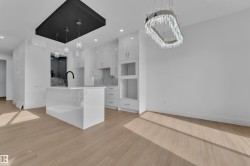 Spacious open-concept kitchen featuring a central island with a matte black faucet, white shaker cabinetry, and a marbled backsplash - 