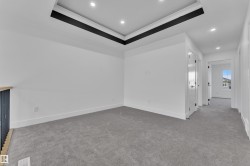 Spacious carpeted room featuring a tray ceiling with recessed lighting, white walls, and a contemporary black railing - 