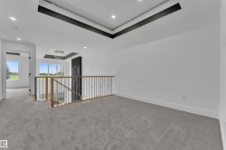 Carpeted loft area featuring a tray ceiling with dark accents, recessed lighting, and a contemporary chandelier - 