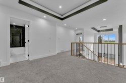 Spacious upper-level landing featuring plush gray carpeting and a black and wood-tone railing system - 