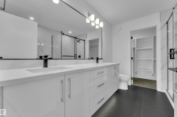 Contemporary bathroom featuring a double vanity with white cabinetry, integrated sinks, and matte black fixtures - 