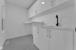 Laundry room featuring white cabinetry with silver hardware, a countertop with an integrated sink and matte black faucet, and a wall-mounted folding surface - 