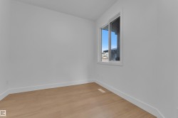 Bright interior room featuring a window with white trim, wood-finish flooring, white baseboards, and clean white walls - 