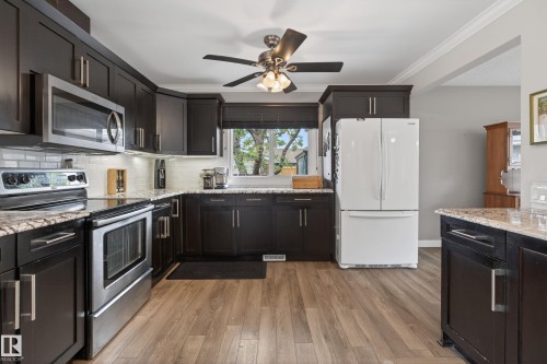 Modern kitchen featuring dark wood cabinetry, stainless steel appliances, light-toned countertops, subway tile backsplash, and wood-finish flooring - 10 Abbey Crescent, St. Albert, AB - Indoor Photo Showing Kitchen With Upgraded Kitchen