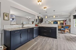 Open-concept kitchen featuring dark cabinetry, speckled countertops, and a white subway tile backsplash - 