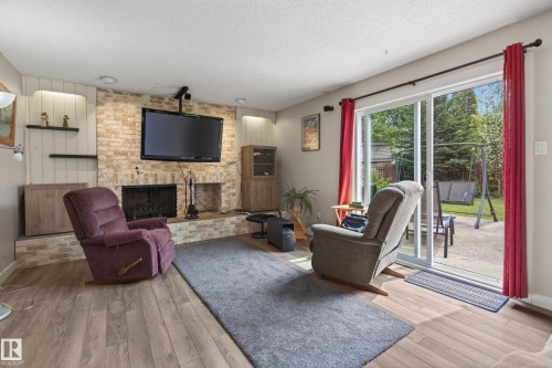 Living area featuring wood-finish flooring, a brick fireplace with hearth, and built-in shelving - 10 Abbey Crescent, St. Albert, AB - Indoor Photo Showing Living Room With Fireplace