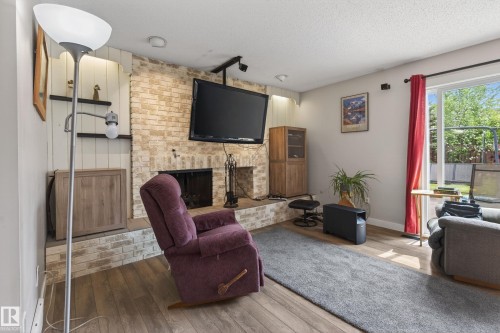 Living area featuring a brick-surround fireplace, wood-finish flooring, and white painted walls - 10 Abbey Crescent, St. Albert, AB - Indoor Photo Showing Living Room With Fireplace