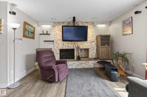 Brick-clad fireplace with a built-in hearth, flanked by recessed shelving and wood-finish flooring - 10 Abbey Crescent, St. Albert, AB - Indoor Photo Showing Living Room With Fireplace