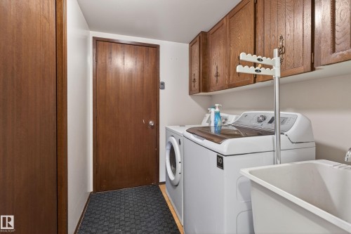 Dedicated laundry area featuring wood-finish flooring, a utility sink, and wall-mounted cabinetry - 10 Abbey Crescent, St. Albert, AB - Indoor Photo Showing Laundry Room
