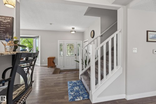 Welcoming entry featuring a white paneled door with decorative glass inserts, wood-finish flooring, a carpeted staircase with white balusters, and light gray wall tones - 10 Abbey Crescent, St. Albert, AB - Indoor Photo Showing Other Room