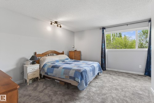 Carpeted bedroom with a large window, light gray walls, and a textured ceiling - 10 Abbey Crescent, St. Albert, AB - Indoor Photo Showing Bedroom