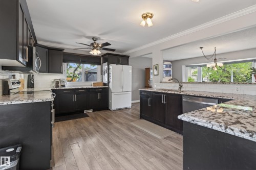 Kitchen featuring dark cabinetry, speckled countertops, a white subway tile backsplash, wood-finish flooring, and a ceiling fan - 10 Abbey Crescent, St. Albert, AB - Indoor Photo Showing Kitchen With Upgraded Kitchen