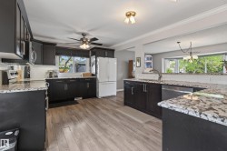 Kitchen featuring dark cabinetry, speckled countertops, a white subway tile backsplash, wood-finish flooring, and a ceiling fan - 