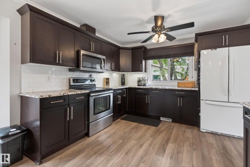 Open-concept kitchen featuring dark wood cabinetry, light granite-style countertops, and a white subway tile backsplash - 10 Abbey Crescent, St. Albert, AB - Indoor Photo Showing Kitchen