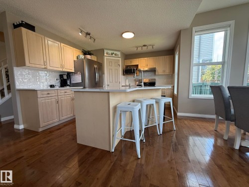Kitchen featuring light wood-finish cabinetry, a central island with countertop seating, stainless steel appliances, and a tiled backsplash - 1820 Robertson Crescent Sw, Edmonton, AB - Indoor Photo Showing Kitchen