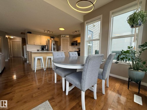 Integrated kitchen and dining area featuring wood-finish flooring, a contemporary circular pendant light, and two large windows - 1820 Robertson Crescent Sw, Edmonton, AB - Indoor Photo Showing Dining Room