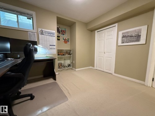 Carpeted room with a built-in closet featuring bi-fold doors, a recessed wall niche, and a window with blinds - 1820 Robertson Crescent Sw, Edmonton, AB - Indoor Photo Showing Office