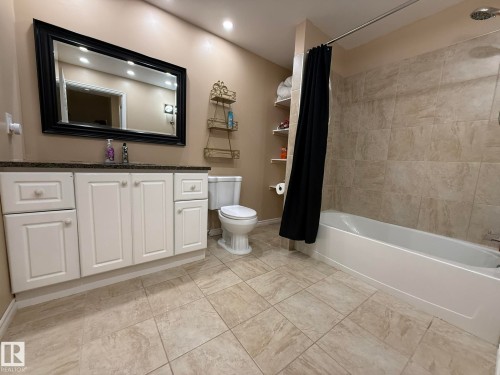 Bathroom featuring a white vanity with a dark countertop, an expansive framed mirror, a tub/shower combination with tile surround, and tile flooring - 1820 Robertson Crescent Sw, Edmonton, AB - Indoor Photo Showing Bathroom