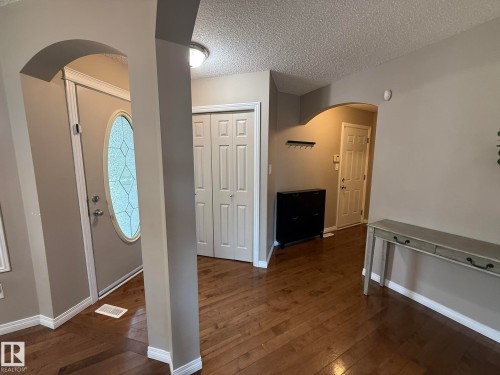 Arched doorway entryway featuring wood-finish flooring, a front door with an oval decorative glass insert, and bi-fold closet doors - 1820 Robertson Crescent Sw, Edmonton, AB - Indoor Photo Showing Other Room
