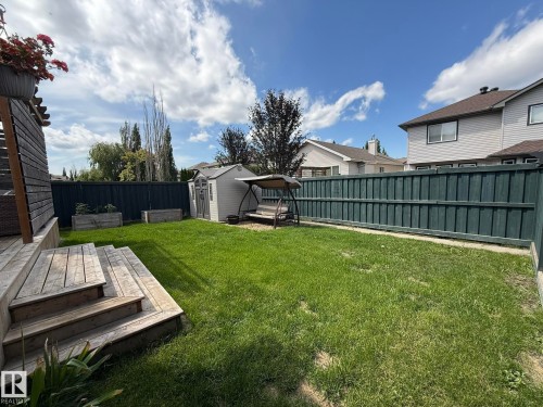 Expansive backyard featuring a lush lawn, privacy fencing, wood deck with stairs, two raised garden beds, and a storage shed - 1820 Robertson Crescent Sw, Edmonton, AB - Outdoor