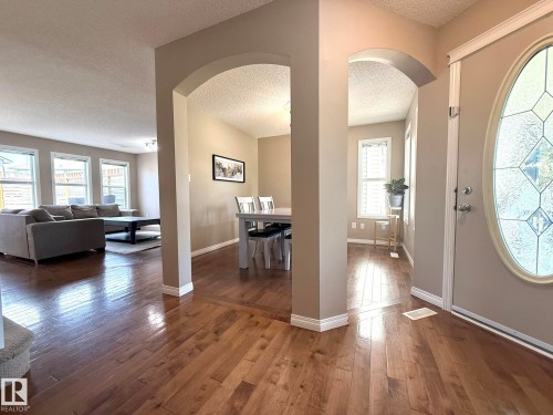 Entryway featuring rich wood-finish flooring extending throughout, a decorative glass-paneled entry door, and arched doorways leading to additional interior spaces - 1820 Robertson Crescent Sw, Edmonton, AB - Indoor