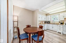 Kitchen featuring white cabinetry, light wood-finish countertops, a window overlooking exterior greenery, white appliances, and wood-finish flooring - 
